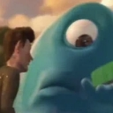A blue one-eyed creature stares intensely at a small green object with a suspicious expression.
