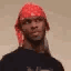 A man wearing a red bandana looking at the camera with a skeptical and confused expression.