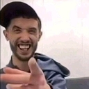 A man with a beard and a baseball cap smiling widely while pointing his finger directly at the camera.