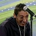 A man with a wide, intense grin speaking into a microphone.