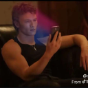 A man looking at his phone with pink, purple, and blue light reflecting on his face.