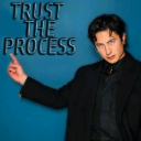 A man in a black suit pointing to the text Trust The Process against a blue background.