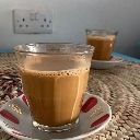 Two glasses of warm brown tea sitting on saucers on a textured mat.