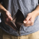 A person holding an open, empty brown wallet with both hands.