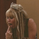 Miley Cyrus wearing a tiara with a disgusted expression and her finger in her mouth.