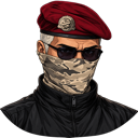 Soldier wearing a red beret, sunglasses, and a camouflage face mask looking forward with a serious expression.