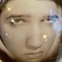A human face distorted by a fish-eye lens, staring intensely with a serious expression.