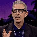 A man wearing glasses and a blazer makes a series of skeptical and contemplative facial expressions.