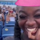A person laughing with a hand near their mouth while wearing a bright pink hat.