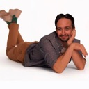 Lin-Manuel Miranda lying on his stomach, propped up on his elbows with a charming smile.