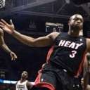 Dwyane Wade in a black Miami Heat jersey reaching out during a basketball game.