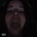 Person with long hair making a silly wide-mouthed expression in low lighting.