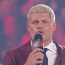 Cody Rhodes in a suit shouting into a microphone with his mouth opening wider across four frames.