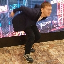 A man wearing a blue blazer and black pants leans forward in a silly, crouched pose.