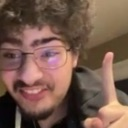 A young man with curly hair and glasses smiling smugly while holding up one finger.