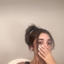 A person covering their mouth with their hand while looking at the camera with a shocked expression.