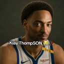 A basketball player with a short haircut wearing a white and blue jersey looks directly at the camera with a confused and se…