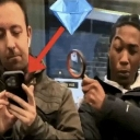 Two men looking intensely at a smartphone while one holds a magnifying glass and a red arrow points to the screen.