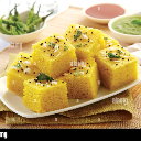 Dhokla squares arranged on a white plate with green chutney in the background.