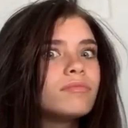 A young woman with dark hair looking at the camera with a skeptical and suspicious facial expression.