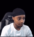 A man wearing a black durag and white t-shirt looking around with a confused and suspicious expression.