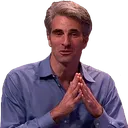 A man with gray hair and a blue shirt sits with his hands pressed together in a steeple gesture.