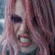 A woman with pink hair and dark eye makeup snarling with her teeth bared in anger.