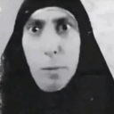 A person wearing a head covering stares intensely with wide, unblinking eyes.