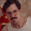 Man with a mustache and glasses looking directly at the camera with a skeptical and disgusted expression.