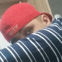 A person wearing a red cap peeks out from behind their arm while looking at the camera.