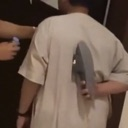 Person standing with a clothing iron pressed against their back.