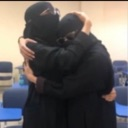 Two people wearing black head coverings and clothing hugging each other tightly.