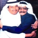 Two men wearing traditional headwear and clothing are hugging each other warmly.