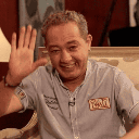 A man smiling and waving his hand in a friendly gesture.