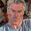 Man with an extremely defined jawline and gray hair looking directly at the camera with a serious, stoic expression.