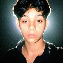 A young person with dark hair looking directly at the camera with a neutral, unimpressed expression against a dark backgro...