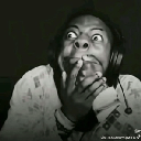 A person with wide eyes covering their mouth in shock while wearing headphones.