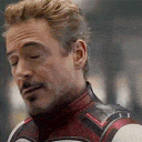 Tony Stark wearing a tactical suit smirks and tilts his head with a smug expression.