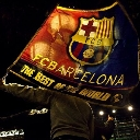 A person holding a large flag with the FC Barcelona crest and text in a dark stadium setting.