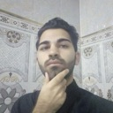 Man with a beard looking at the camera with his hand resting on his chin in a thoughtful pose.