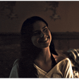 Woman with long dark hair smiling with a subtle, mysterious expression in low-key lighting.