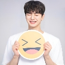 Young man with dark hair smiling while holding a yellow circular sign with a laughing emoji face.