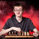 Young man with glasses playing chess with a smug expression against a red smoky background.
