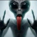 Alien with large black eyes presses its face and tongue against a glass surface with hands visible on both sides.