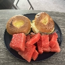 A black plate holding two bagels and several cubes of fresh red watermelon.