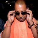 A man wearing orange clothing adjusts his dark sunglasses with both hands while looking down with a serious expression.