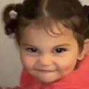 A toddler with pigtails giving a sly, mischievous smirk.