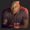 A man with a shaved head and a mustache stares intensely while holding a plastic cup.