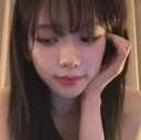 A young woman looking down with a shy, bashful expression while resting her chin on her hand.