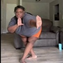 A person in a gray shirt and orange shorts performing a dynamic, mid-air dance move.